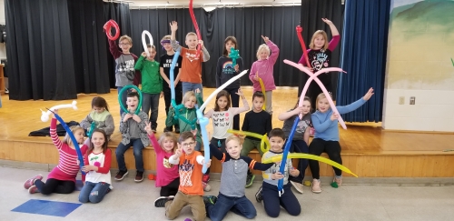 group of 20 children pose for photo in front of small stage holding balloon shaped into animals
